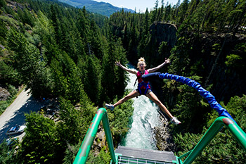 view from jumping point with spread eagle jumping women on bungee cord, creek and trees below