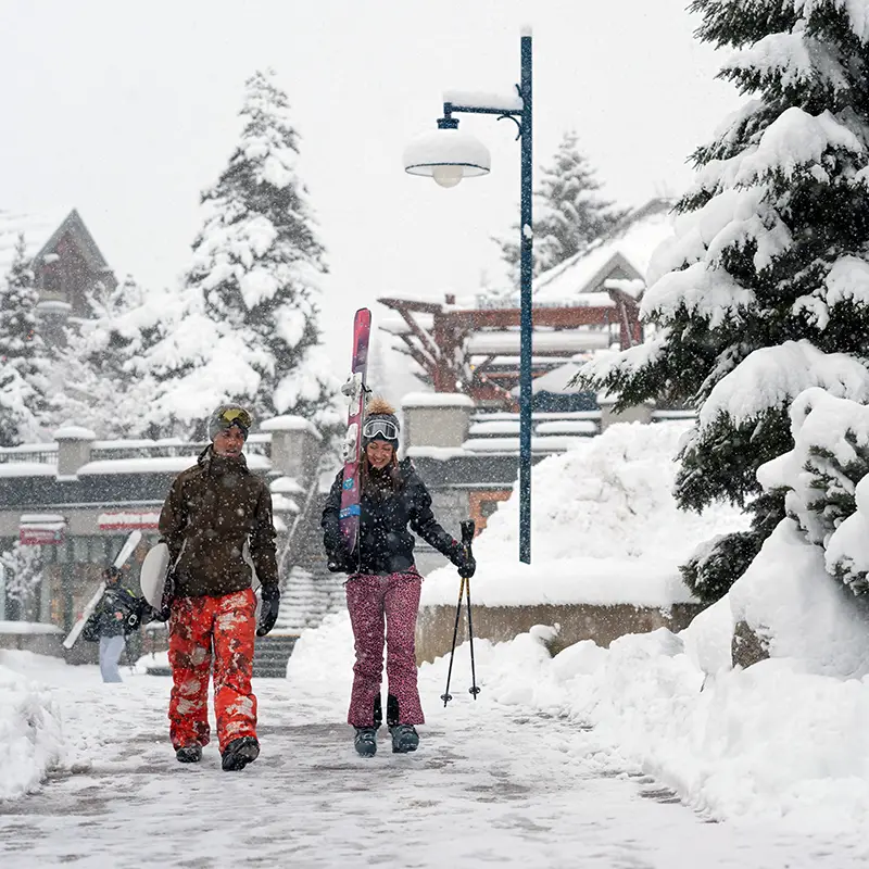 Skier and snowboarder walking through village to lifts on a powder day!