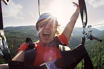 smiling happy women with hand up in the air in harness with mountain views behind